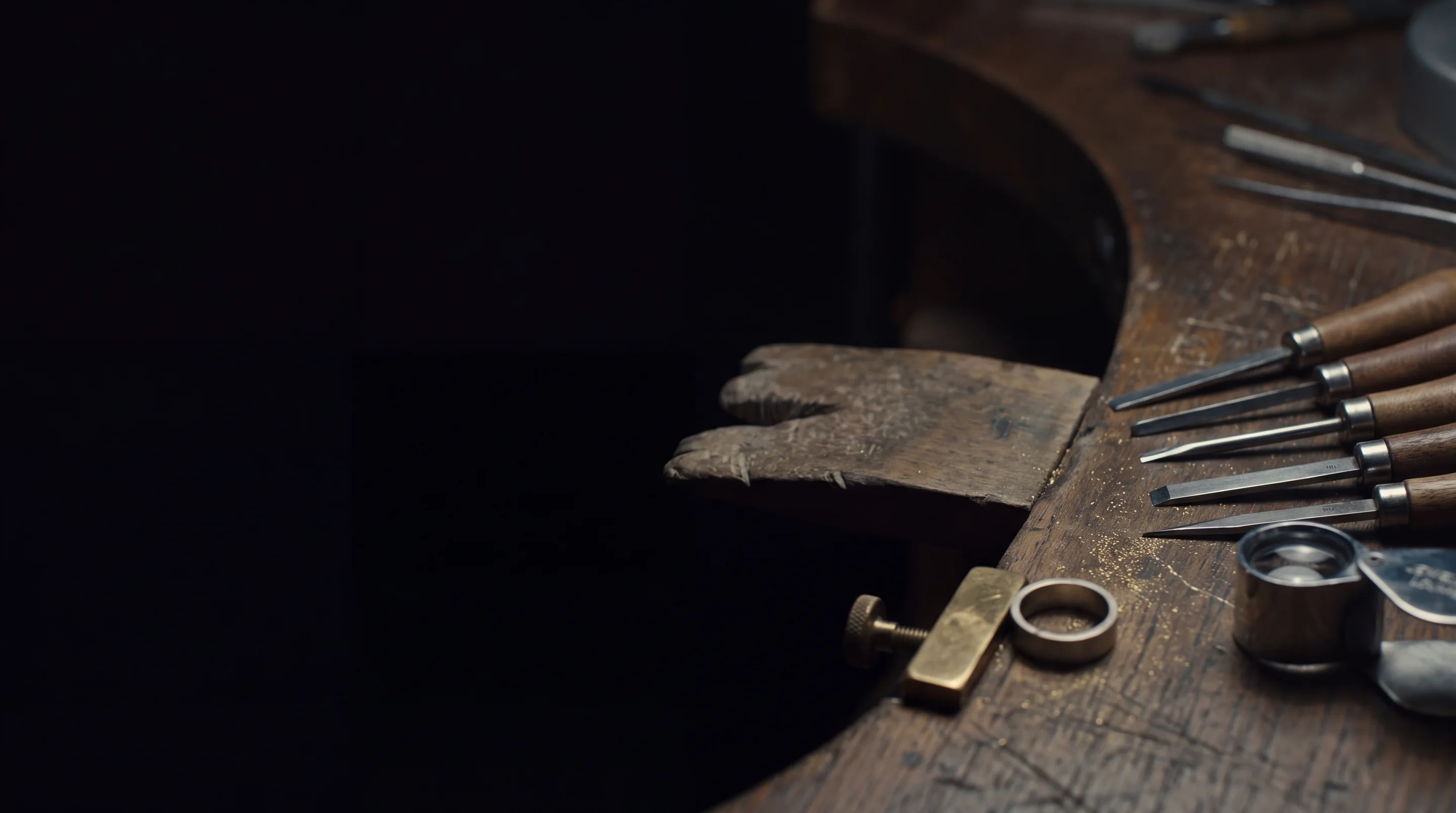 Un établi de joaillier la nuit : cheville, échoppes alignées, pince de laiton tenant un anneau brut, loupe, poussière d’or sur le bois. Image générée du métier — aucune pièce de collection, aucune maison identifiable, aucun travail livré.